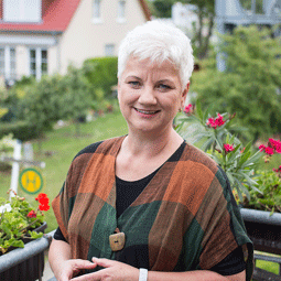 Marion Petersdorf steht im Freien vor Blumen und lächelt