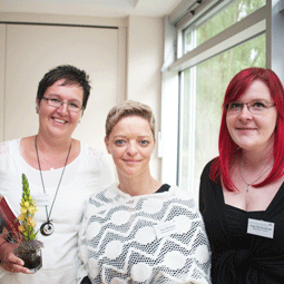 Lucienne Smolibowski mit zwei Mitarbeiterinnen und hält Blumen in der Hand